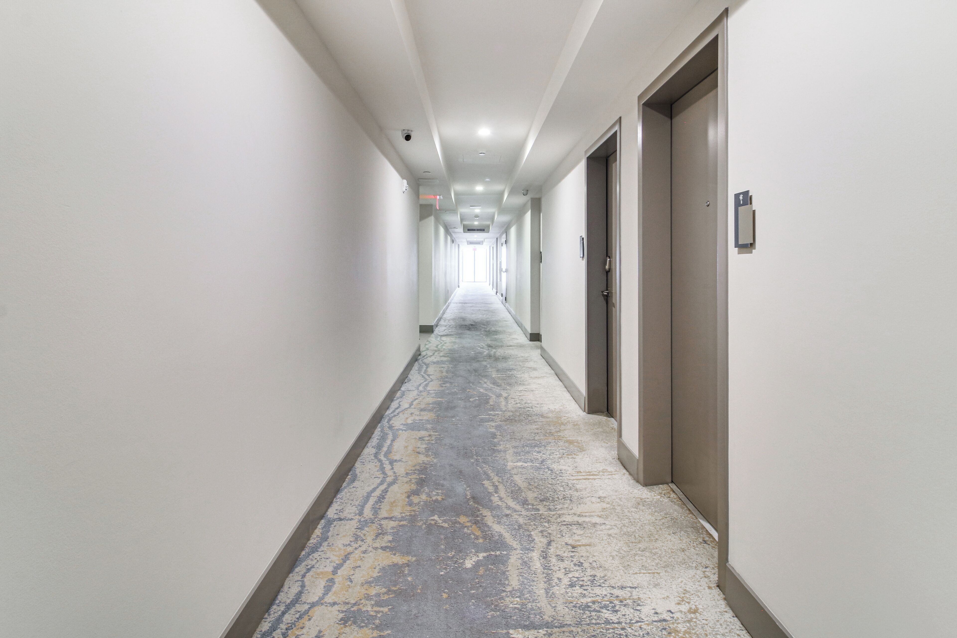 A long, narrow hotel corridor with doors on one side and a patterned carpet.