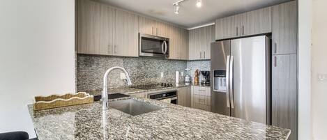 A modern kitchen with granite countertops, stainless steel appliances, and wooden cabinetry.