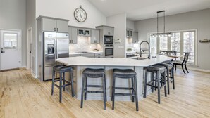 Une cuisine moderne dotée d’un îlot central, de tabourets de bar, d’une horloge et d’une grande fenêtre.