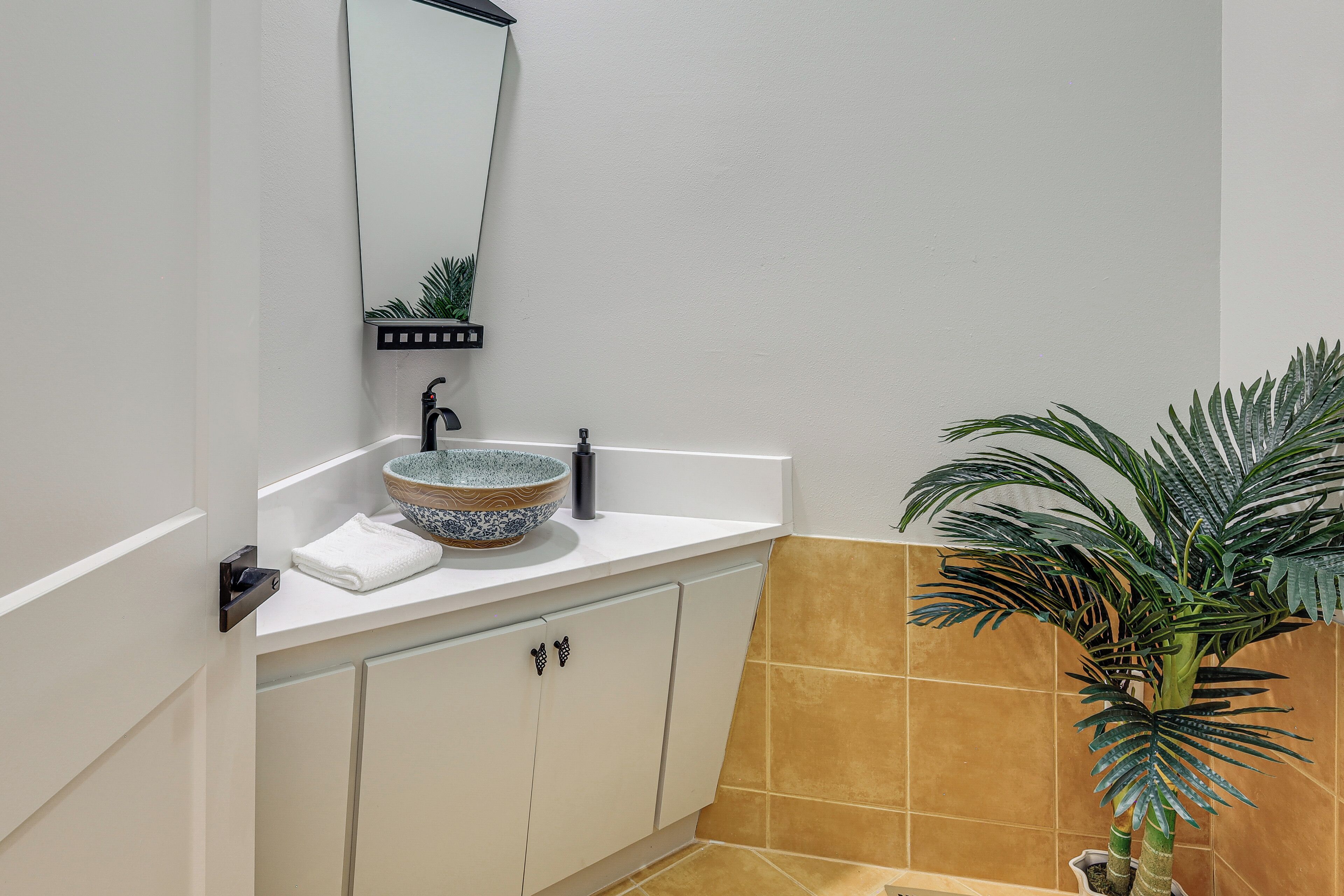 A bathroom with a white sink, a mirror, a towel, a potted plant, and a tiled wall.