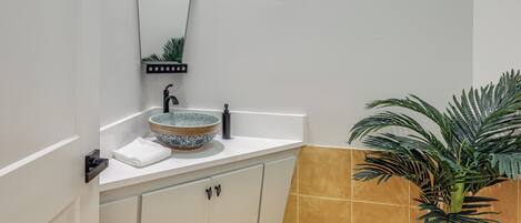 A bathroom with a white sink, a mirror, a towel, a potted plant, and a tiled wall.