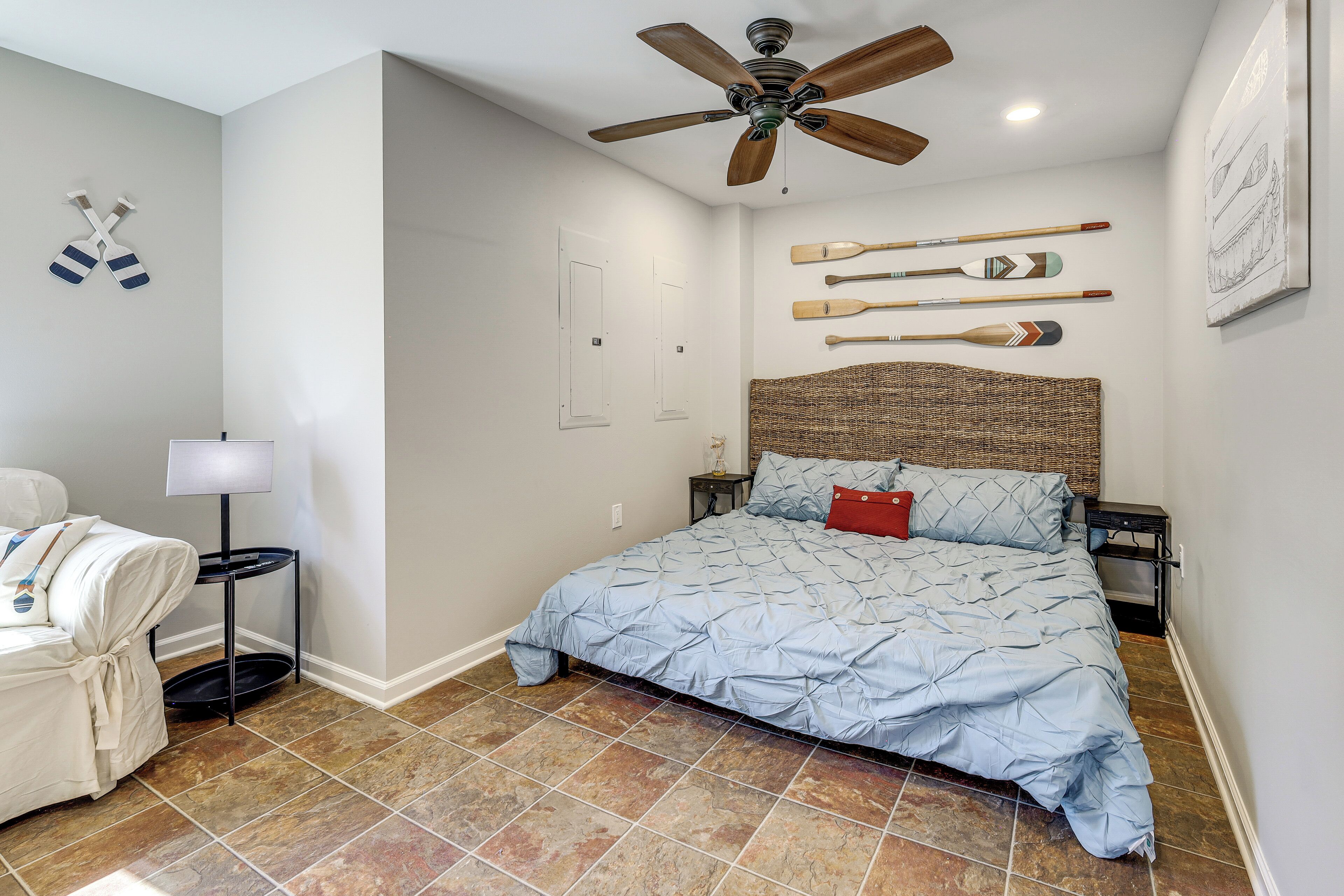 A bedroom with a bed, a ceiling fan, a wall-mounted lamp, and a wall with paddleboards.