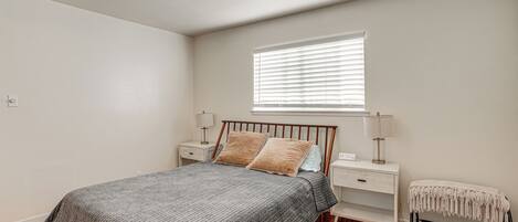 Un dormitorio con cama, mesitas de noche, un banco, una ventana y una lámpara en el techo.