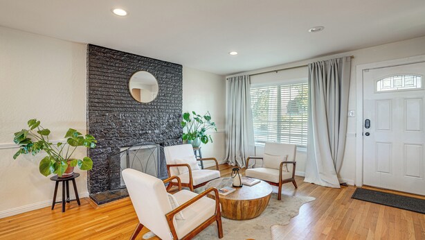 A living room with a fireplace, wooden flooring, and a white door. - Bay Area Family Home w/ Indoor Pool + Game Room (South San Francisco)