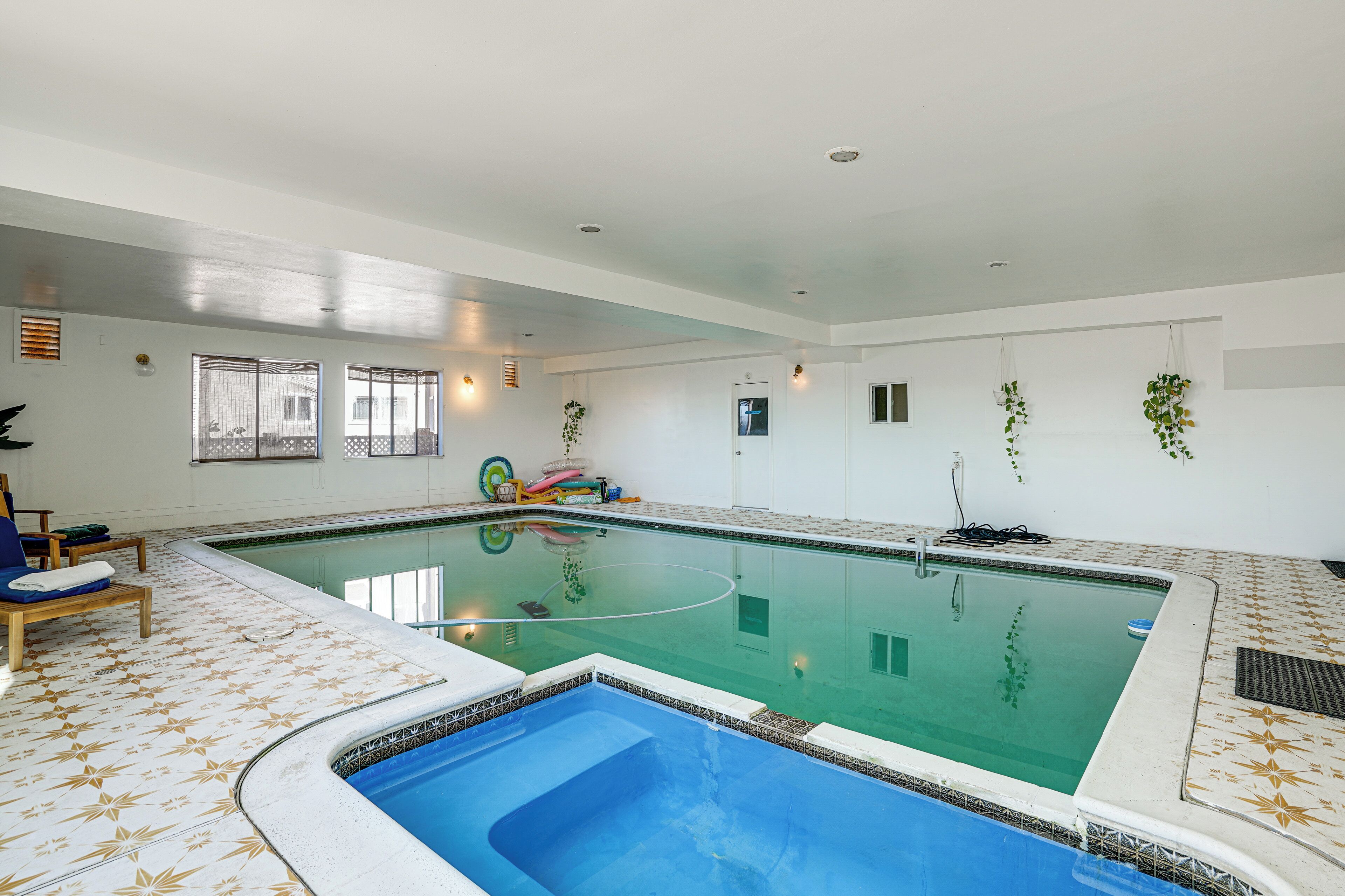 Una piscina interior con suelo de baldosas, una zona de piscina más pequeña y una puerta que da a otra habitación.