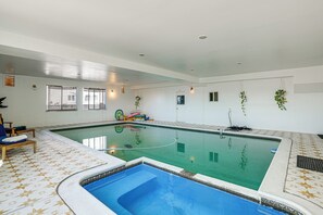 An indoor swimming pool with a tiled floor, a smaller pool area, and a door leading to another room. - Bay Area Family Home w/ Indoor Pool + Game Room (South San Francisco)