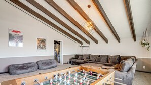 A room with a foosball table, a sofa, and a ceiling with exposed beams. - Bay Area Family Home w/ Indoor Pool + Game Room (South San Francisco)