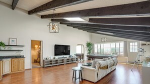 A spacious living area with a large TV, wooden flooring, a sofa, and a dining table.