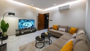 Ein modernes Wohnzimmer mit Flachbildfernseher, Sofa, Couchtisch und einer Zimmerpflanze.