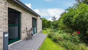 A brick building with a patio, a green door, and a small table and chair. - Casa Wohnen und Wellness: Private Terrace, Garden, Wi-Fi, Direct Forest Access (Hemer)
