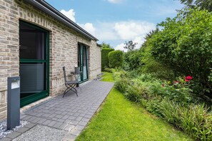 Een bakstenen gebouw met terras, een groene deur en een kleine tafel en stoel.