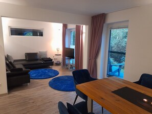 A modern living room with a sofa, a coffee table, and a TV. There is a balcony with a table and chairs. - Holiday Home 'Casa Living and Wellness' with Private Terrace, Garden and Wi-Fi (Hemer)