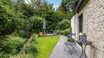 A garden patio with a brick pathway, a table with chairs, and a stone building.