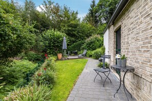 A garden patio with a brick pathway, a table with chairs, and a stone building.