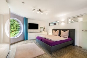 A modern bedroom with a bed, a TV, a window, and a mirror.