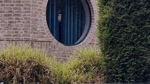 A building with a brick facade, a circular window, and a hedge. - Casa Wohnen und Wellness: Private Terrace, Garden, Wi-Fi, Direct Forest Access (Hemer)