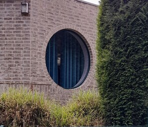 Een gebouw met een bakstenen gevel, een rond raam en een haag.