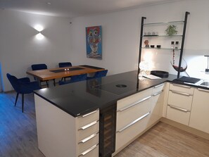 A modern kitchen with a central island, a dining area with blue chairs, and a painting on the wall. - Holiday Home 'Casa Living and Wellness' with Private Terrace, Garden and Wi-Fi (Hemer)