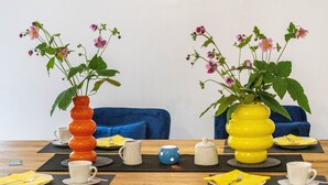 A dining table with two vases of flowers, a blue sofa, and a wooden table surface. - Casa Wohnen und Wellness: Private Terrace, Garden, Wi-Fi, Direct Forest Access (Hemer)