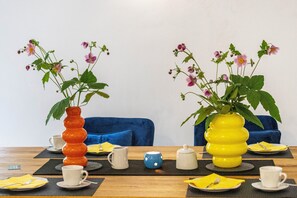 Een eettafel met twee vazen vol bloemen, een blauwe bank en een houten tafelblad.