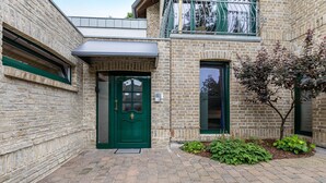 A brick building with a green door, a small garden with plants, and a window with a view. - Casa Wohnen und Wellness: Private Terrace, Garden, Wi-Fi, Direct Forest Access (Hemer)