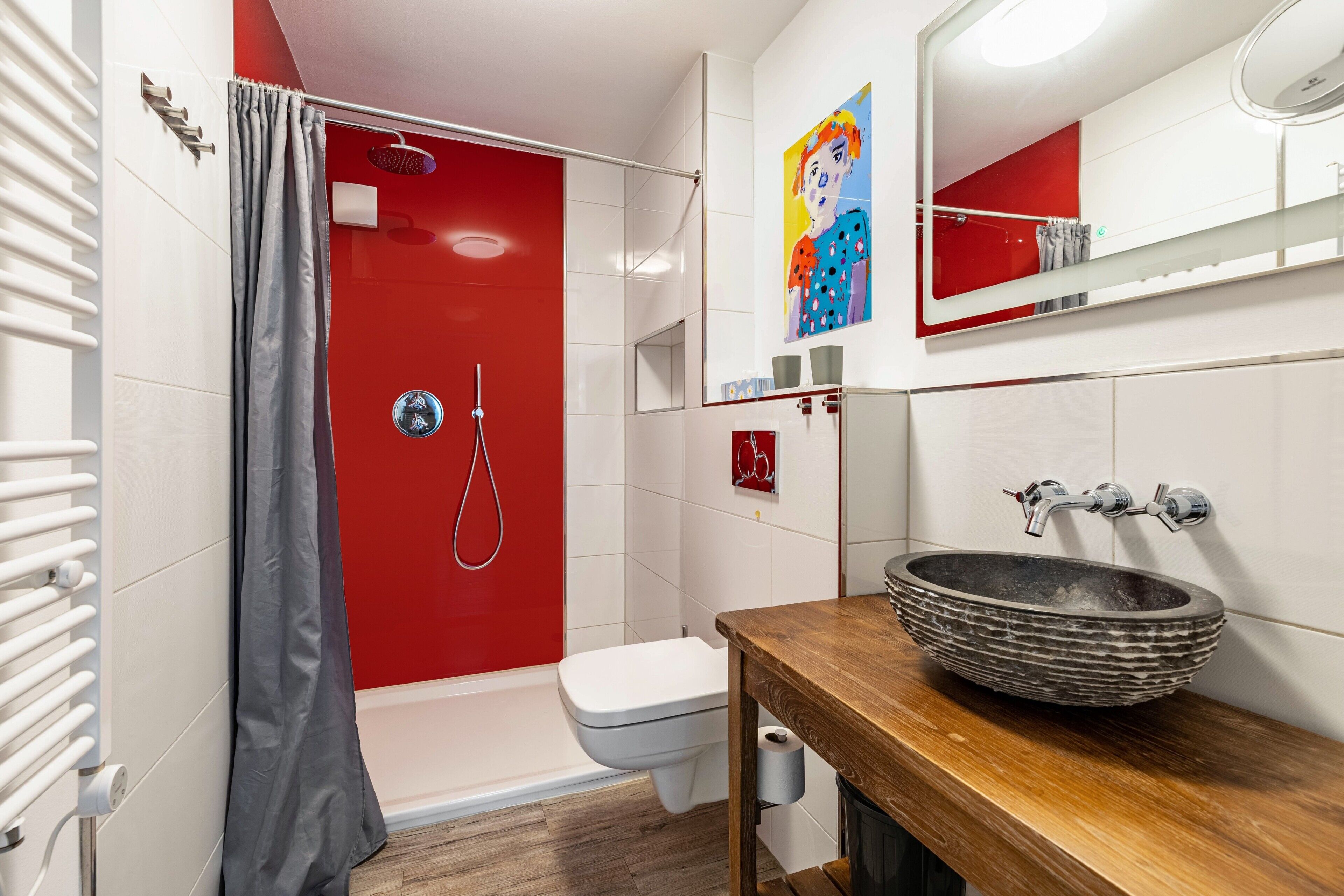Ein Badezimmer mit einer roten Duschkabine, einer weißen Toilette, einem hölzernen Waschtisch mit einem großzügigen Aufsatzbecken und einem Spiegel über dem Waschbecken.