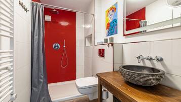 Ein Badezimmer mit einer roten Duschkabine, einer weißen Toilette, einem hölzernen Waschtisch mit einem großzügigen Aufsatzbecken und einem Spiegel über dem Waschbecken.