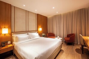 Ein Hotelzimmer mit einem großen Bett, zwei Nachttischlampen, einem Schreibtisch mit Stuhl und einem fenster mit Vorhängen.