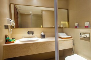 Ein Badezimmer mit Waschbecken, Spiegel, Handtuchhalter und Duschbereich.