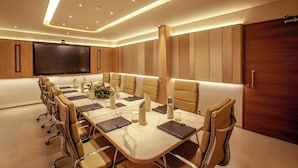A conference room with a long table, chairs, a screen, and a wooden panel wall. - Purple Elephant Luxury Business Hotel (Kanayannur)