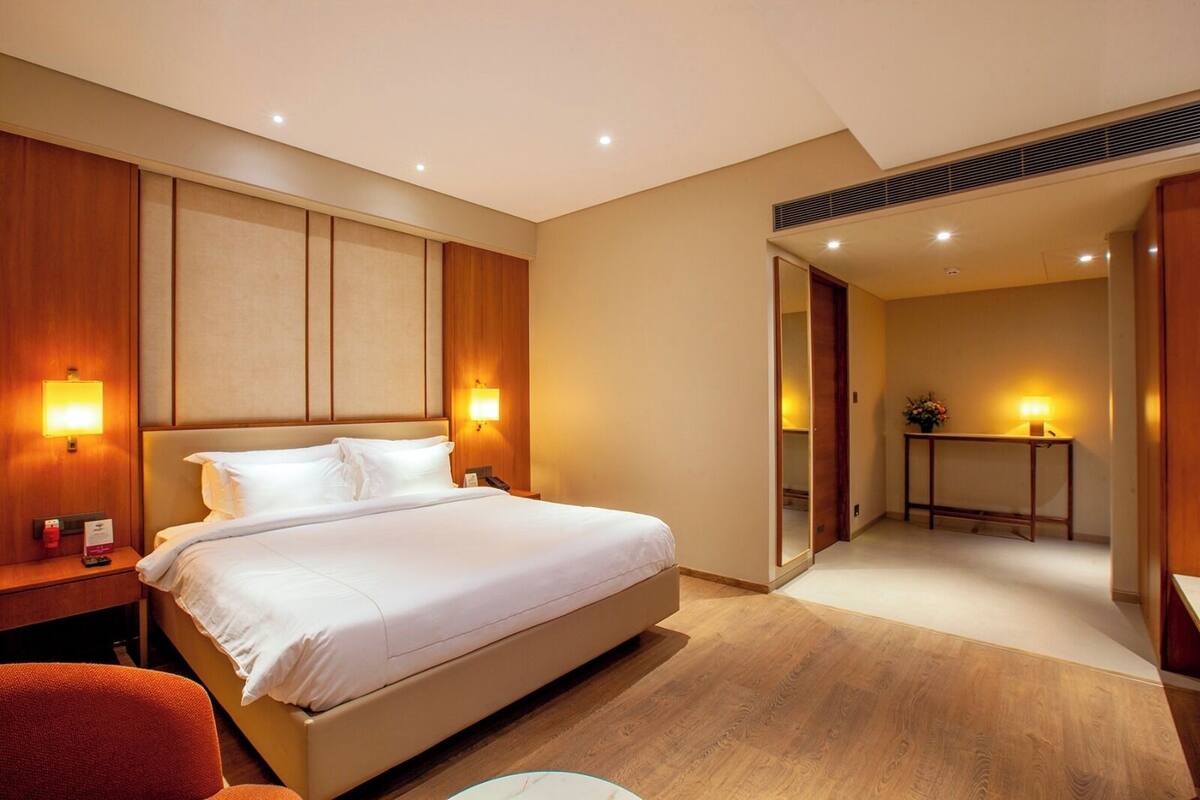 Een hotelkamer met een groot bed, bedlampen, een houten hoofdbord, een nachtkastje en een rode stoel.