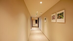 A hallway with a light-colored carpet, recessed ceiling lights, and framed artwork on the walls. - Purple Elephant Luxury Business Hotel (Kanayannur)
