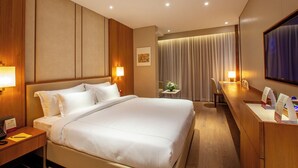 A hotel room with a large bed, bedside tables, a desk, and a television. - Purple Elephant Luxury Business Hotel (Kanayannur)