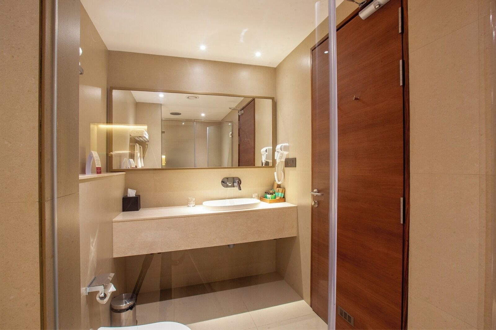 A modern bathroom with a large mirror, a sink, a shower, and a toilet.