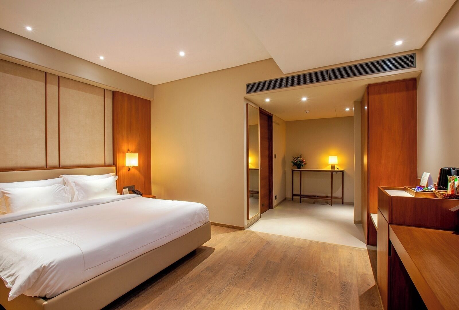 A hotel room with a large bed, bedside lamps, a desk, and a mirror.