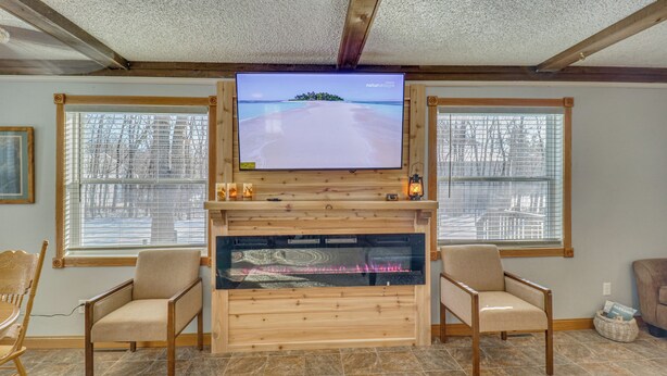 A living room with a fireplace, two chairs, a television, and a large window. - The Farm by the Chain of Lakes: Walk to the Beach! (Alexandria)