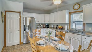 A kitchen with white cabinets, a stainless steel refrigerator, a dining table set with plates, glasses, and a vase of flowers. - The Farm by the Chain of Lakes: Walk to the Beach! (Alexandria)