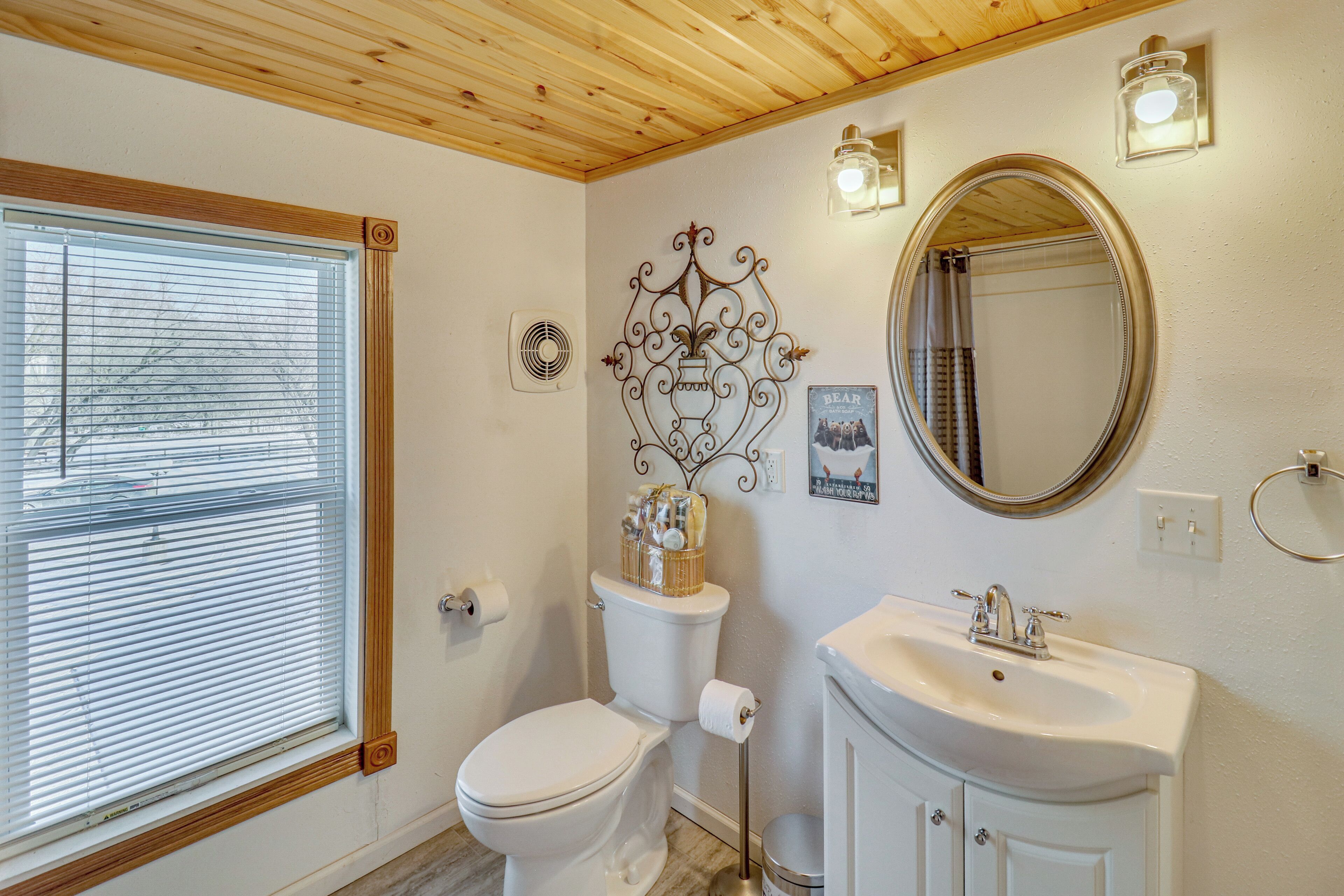 A bathroom with a toilet, sink, mirror, and decorative wall piece.