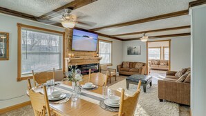 A dining area with a wooden table set for four, a television mounted above the fireplace, and a living room with a sofa and a coffee table. - The Farm by the Chain of Lakes: Walk to the Beach! (Alexandria)