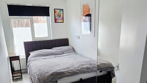 Ein Schlafzimmer mit Bett, Fenster, Heizkörper, Tür und einer Wandleuchte.
