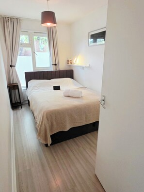 Ein Schlafzimmer mit einem Bett, einem Nachttisch, einer Lampe und einem Fenster mit Vorhängen.