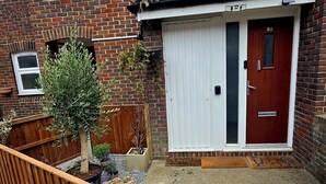 Ein Wohnhaus mit Ziegelverkleidung, einer roten Tür und einem kleinen Garten mit Blumentöpfen.