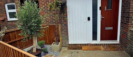A residential property with a brick facade, a red door, and a small garden area with potted plants.