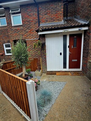 A residential property with a brick facade, a red door, and a small garden area with potted plants. - Cosy flat in Clapham area. Great links ( tube, train, buses) to central. (London)
