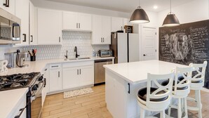 A modern kitchen with white cabinets, a central island, pendant lighting, and a chalkboard wall with a shopping list. - Near Golf, Parks & Casino! Updated Maricopa Home (Maricopa)
