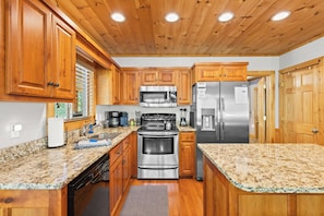 A kitchen with wooden cabinets, granite countertops, stainless steel appliances, and a window with blinds. - < 1 Mi to Lake Blue Ridge: Forest-view Gem w/ Deck (Morganton)