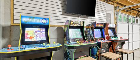 Arcade machines with 'The Simpsons' and 'Turtles' games, a TV above, and wooden stools.
