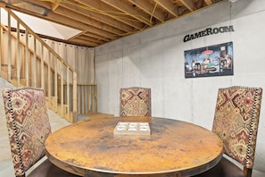 A room with a round wooden table, patterned chairs, a staircase, and a wall sign reading 'GAMEROOM'. - < 1 Mi to Lake Blue Ridge: Forest-view Gem w/ Deck (Morganton)