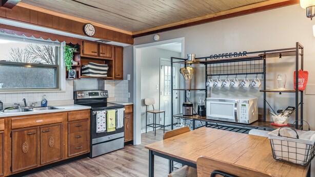 A kitchen with wooden cabinets, a stainless steel stove, a coffee bar with mugs, and a dining table. - Warren County Launchpad: Pet-friendly Lebanon Apt (South Lebanon)