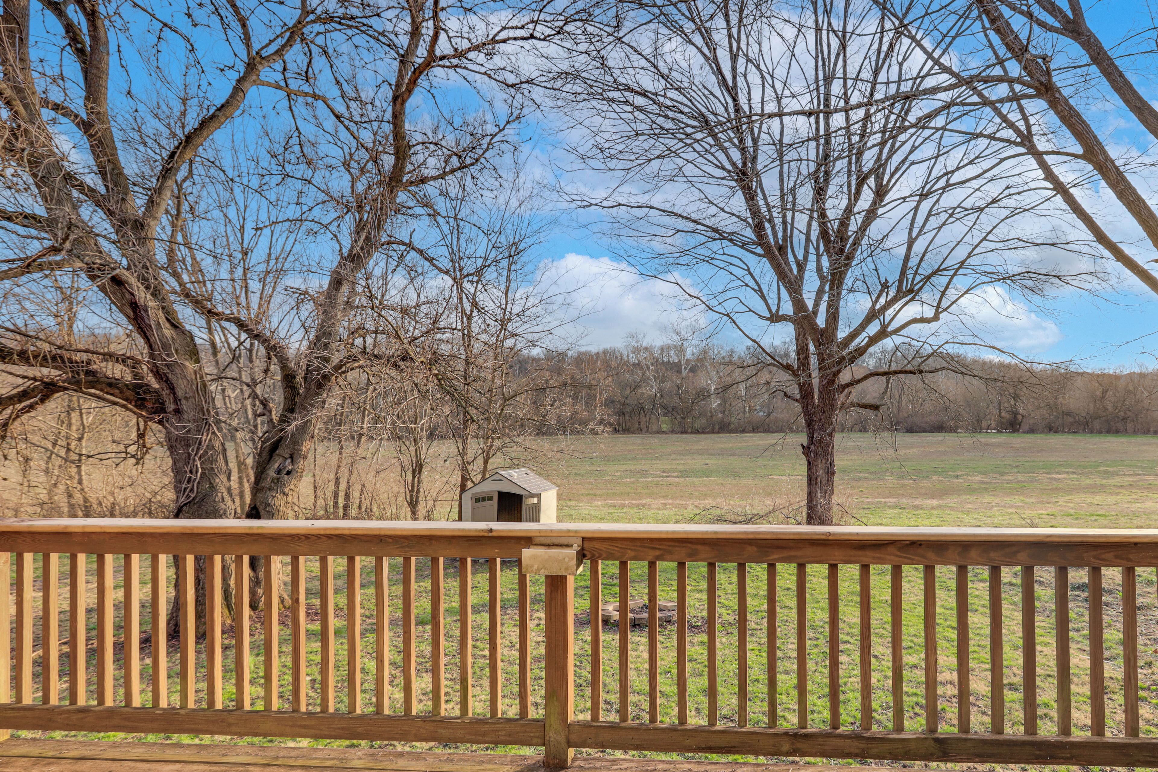 A wooden deck with a view of a grassy field and leafless trees.